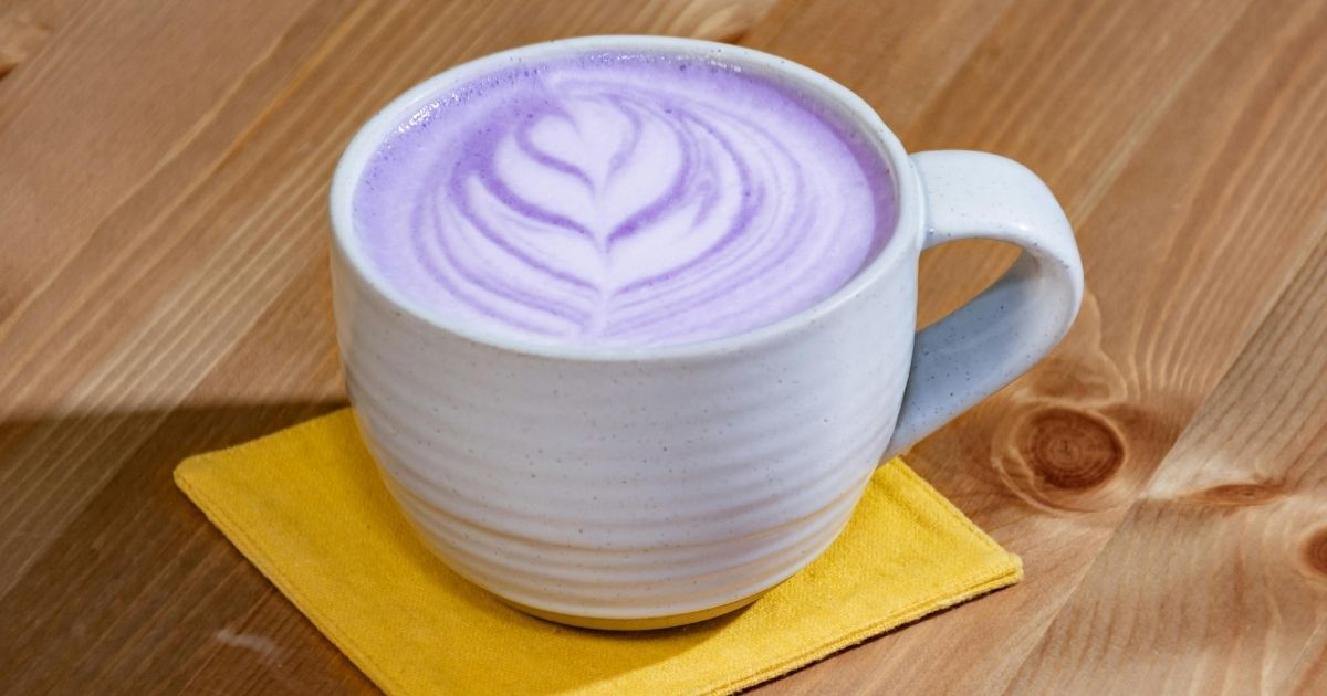 A vibrant purple ube latte in a clear glass showing layered purple and white colors